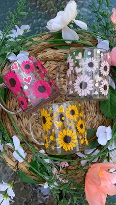 three coffee mugs sitting on top of a wicker basket next to pink and yellow flowers