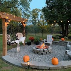 an outdoor fire pit surrounded by chairs and lights with pumpkins on the ground next to it