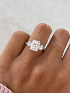 a woman's hand with a diamond ring on top of her finger and the other hand holding an engagement ring