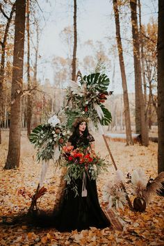 a woman dressed in black with flowers and feathers standing next to a pile of leaves