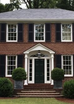 a large brick house with black shutters and white trim on the front entrance steps