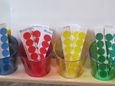 four cups with different colored paper straws in them sitting on a wooden shelf next to each other