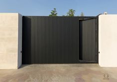 an open gate in the middle of a concrete area with two walls and trees behind it