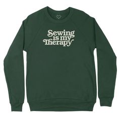 a green sweatshirt with the words sewing is my therapy printed on it in white letters