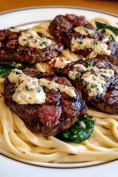 steak with sauce and spinach on top of pasta in a white plate sitting on a wooden table