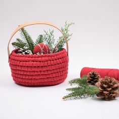 a red basket filled with pine cones next to a small christmas tree branch and cone