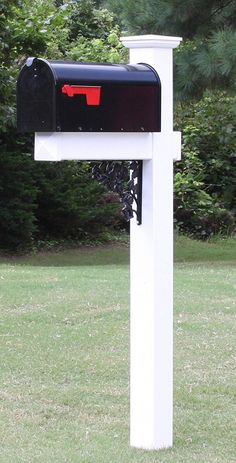 a mailbox in the middle of a grassy area with trees and bushes behind it