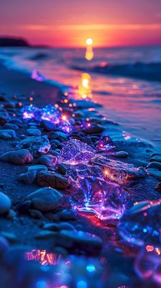 the sun is setting over the water and rocks on the beach with lights in them