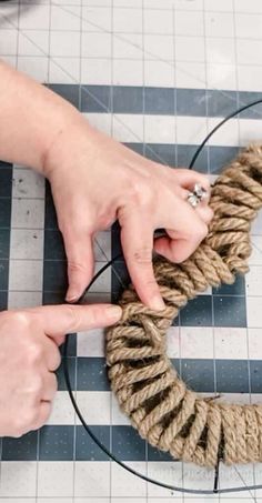 two hands are tying a rope around a ring on a table with black and white checkered flooring