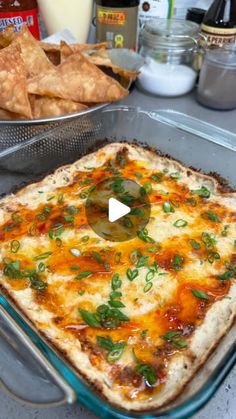 a glass casserole dish filled with cheese, sauce and green onions next to tortilla chips