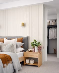 a bedroom with a bed, nightstand and closet in the back ground is white striped walls