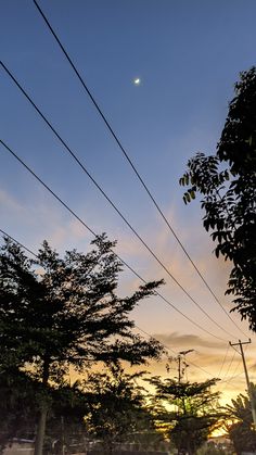 the sun is setting behind power lines and telephone poles with trees in the foreground