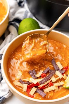 a spoonful of soup in a bowl with tortilla chips and limes on the side