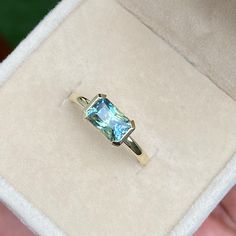 someone is holding a ring with a blue topazte stone in it's box