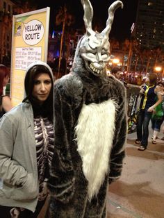 a woman standing next to a man in a bunny costume on the street at night