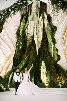 two people standing next to each other in front of a wall covered with greenery