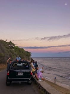 a group of people standing on the side of a road next to a car near the ocean