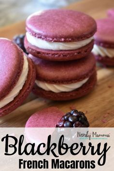 three pink macarons with white frosting and blackberries in the middle on a wooden cutting board