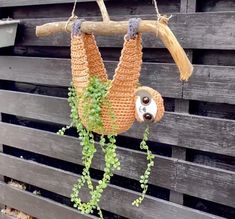 a crocheted sloth hanging from a tree branch with green leaves on it