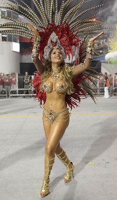 a woman dressed in gold and red is walking down the street with feathers on her head