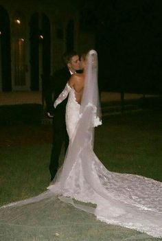 a bride and groom kissing in front of a building at night with the lights on