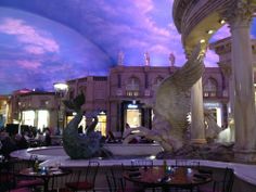 the inside of a building with many tables and chairs around it in front of a fountain