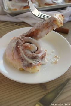 a cinnamon roll on a plate with a fork sticking out of the top, ready to be eaten