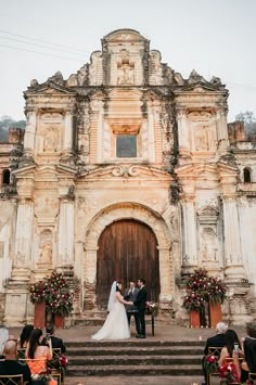 a bride and groom are standing in front of an old church with flowers on the steps