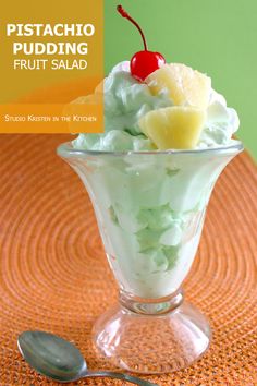 a dessert in a glass bowl with fruit on top and a spoon next to it