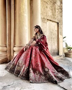 a woman in a red and gold wedding dress sitting on the ground next to columns