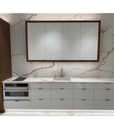 a white kitchen with marble counter tops and cabinets in the back wall, along with a large mirror over the sink