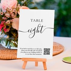 a table sign sitting on top of a wooden easel next to a vase filled with flowers