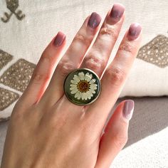 a woman's hand holding a ring with a flower on it and a cushion behind her