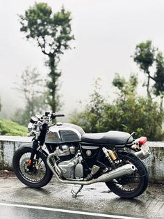 a motorcycle parked on the side of a road in the rain with trees behind it