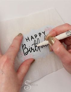 a person is writing on a piece of paper with a white marker that says happy birthday