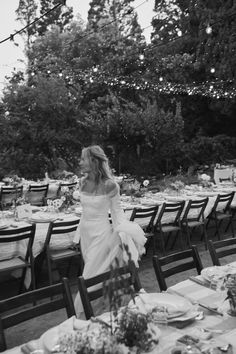 black and white photograph of a woman in a wedding dress walking down the aisle at a dinner table