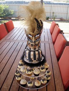 a wooden table topped with cupcakes and a fancy mask on top of it