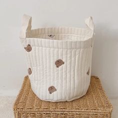 a white basket sitting on top of a wicker stool next to a brown teddy bear