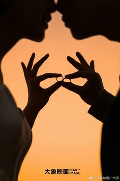 the silhouette of two people making a heart shape with their hands