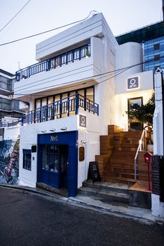 a white and blue building with stairs leading up to it's second floor on the street