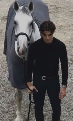 a man standing next to a white horse with a black cover on it's head