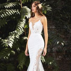 a woman standing in front of some plants wearing a white wedding dress with sheer lace