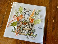 a close up of a card with carrots and a bunny in a basket on a wooden table