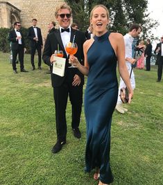 a woman in a blue dress holding an orange drink and standing next to a man in a tuxedo