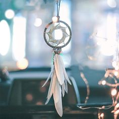 a car dashboard with a white dream catcher hanging from it's center console and lights in the background