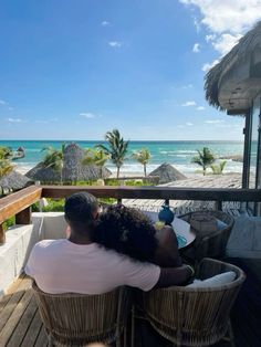 a man and woman sitting on top of a wooden deck next to the ocean with palm trees