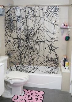 a white toilet sitting next to a bath tub covered in black spider webs on the shower curtain