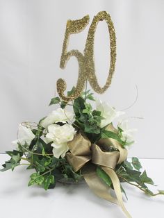 a 50th birthday cake topper with flowers and greenery in front of the number 50