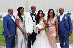 a group of people standing next to each other in front of a white wall and grass