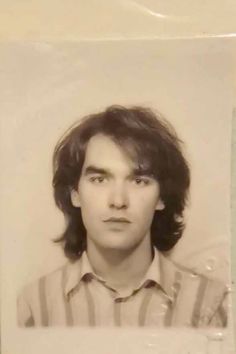 an old black and white photo of a man with long hair wearing a striped shirt